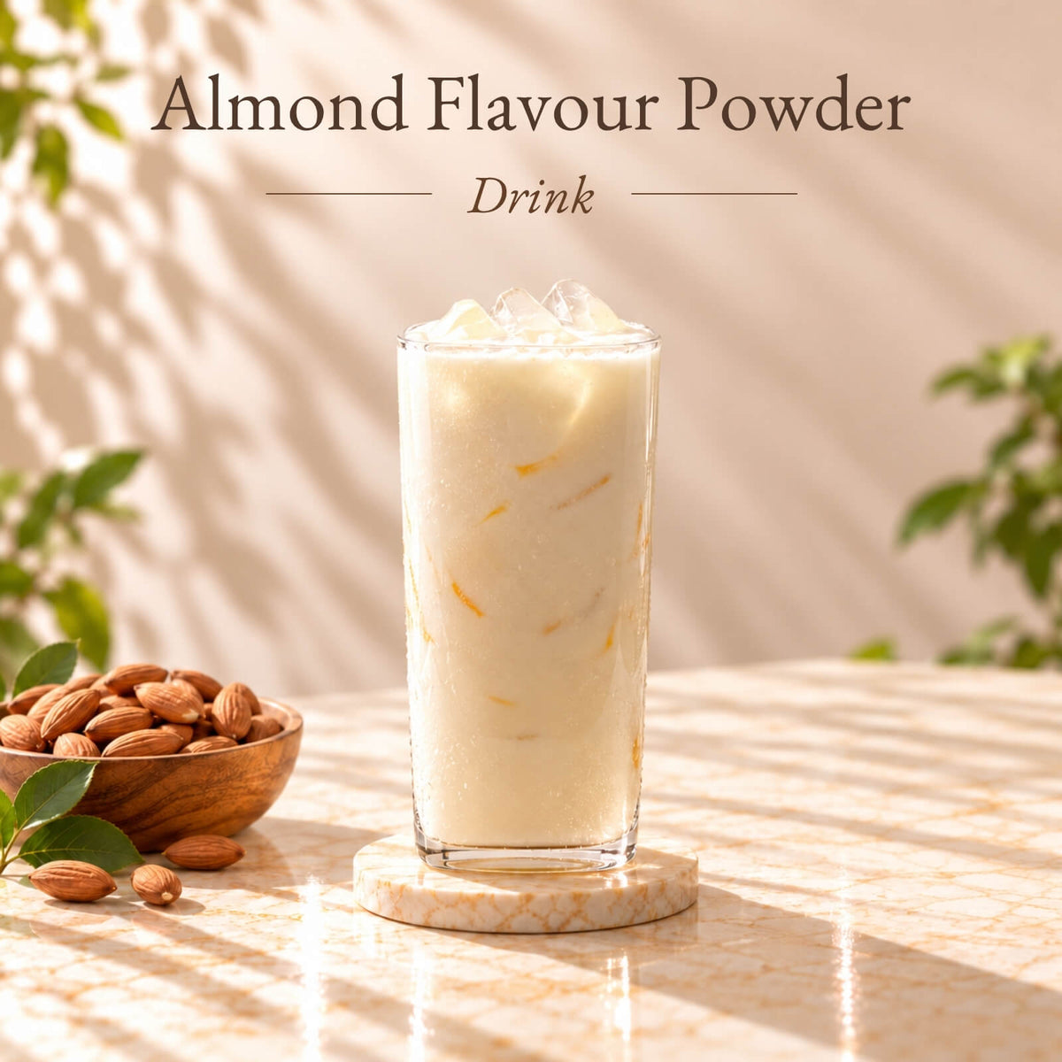 Creamy iced almond flavoured drink served in a tall clear glass with ice cubes, surrounded by almonds on a warm beige marble surface.