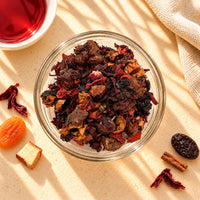 Black Forest Fruit Tea blend in a glass bowl, showing dried roselle, rose hips, raisins and mixed dried fruit pieces in red, brown and orange tones.