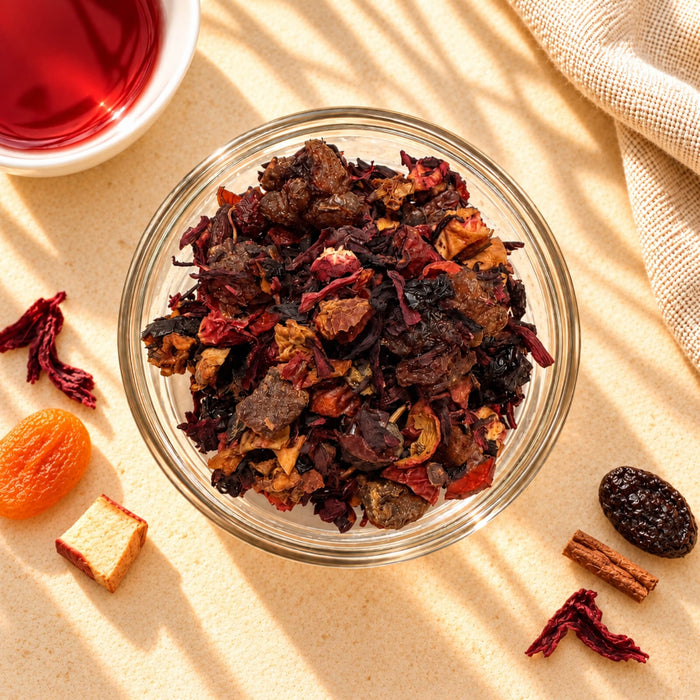 Black Forest Fruit Tea blend in a glass bowl, showing dried roselle, rose hips, raisins and mixed dried fruit pieces in red, brown and orange tones.