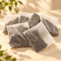 Six rectangular 10g Blueberry Black Tea bags made from fine filter material, showing dark tea leaves inside, arranged on a warm beige surface.