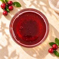 Cranberry flavoured syrup in a glass bowl, showing its deep ruby-red colour and glossy texture, displayed alongside fresh cranberries.
