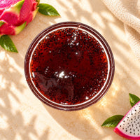 Dragon fruit flavoured syrup in a glass bowl, showing its deep red colour, glossy texture and visible black seeds, displayed alongside fresh dragon fruit.