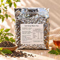 600g package of Earl Grey Black Tea in a silver foil bag with a product label, displayed alongside loose black tea leaves and a cup of brewed tea.