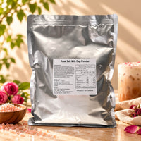 Himalayan Pink Salt Milk Foam Powder in a 1kg silver foil package, displayed with pink salt crystals, roses and a milk foam topped drink in natural sunlight.