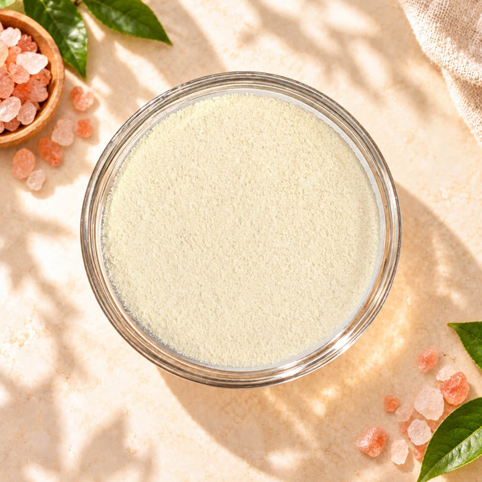 Top view of Himalayan Pink Salt Milk Foam Powder in a clear glass bowl, showing its fine creamy texture, surrounded by pink salt crystals on a warm beige background.