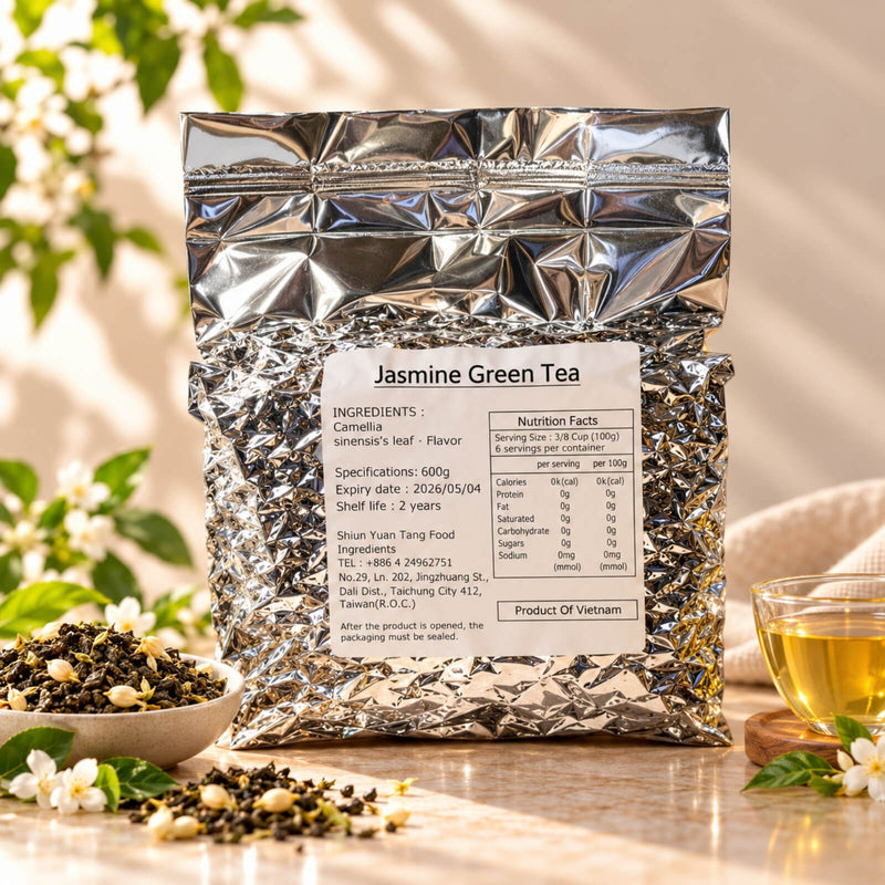 600g package of Jasmine Green Tea in a silver foil bag with a product label, displayed alongside loose green tea leaves, jasmine flowers and a cup of brewed tea.