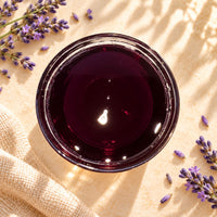 Lavender flavoured syrup in a glass bowl, showing its deep purple-red colour and smooth, glossy texture, surrounded by lavender flowers.