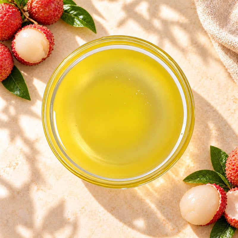 Lychee flavoured syrup in a glass bowl, showing its translucent golden-yellow colour, displayed with fresh lychees.