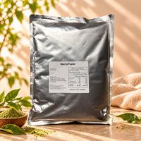 Matcha Powder in a 1kg silver foil package with a product label, displayed alongside a small wooden bowl of green matcha powder under warm natural sunlight.