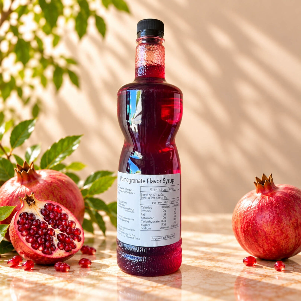 Bottle of Pomegranate Flavoured Syrup with deep red syrup and a black screw cap, displayed alongside whole and cut pomegranates.