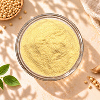 Top view of Soy Milk Powder in a clear glass bowl, surrounded by natural soybeans and green leaves on a warm beige background.r