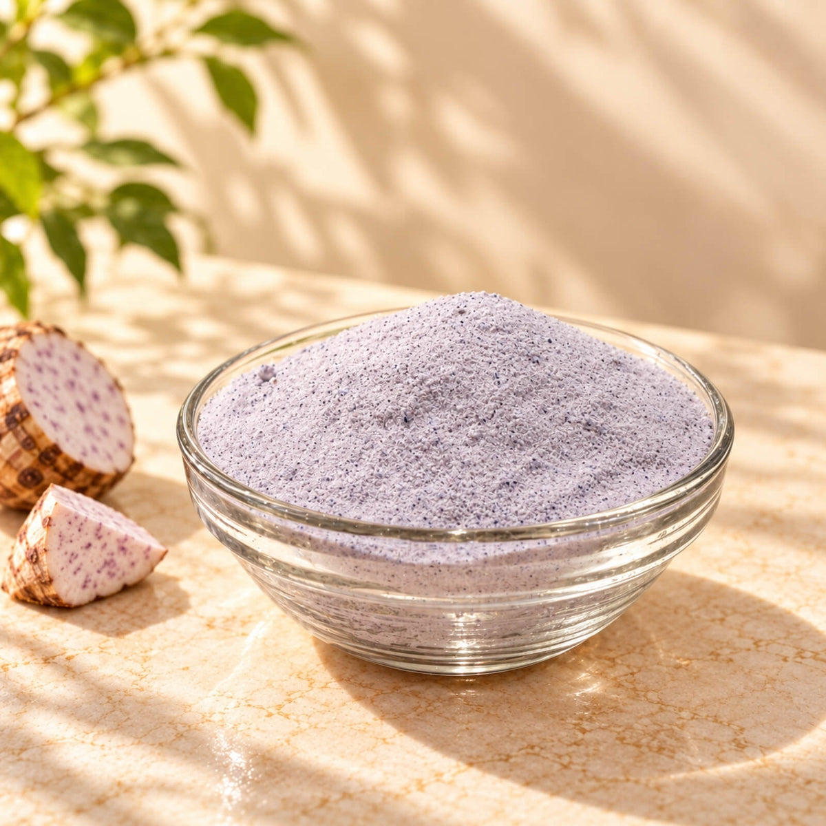 Fine, light purple taro powder piled in a clear glass bowl, displayed with fresh taro roots and slices under warm natural sunlight.